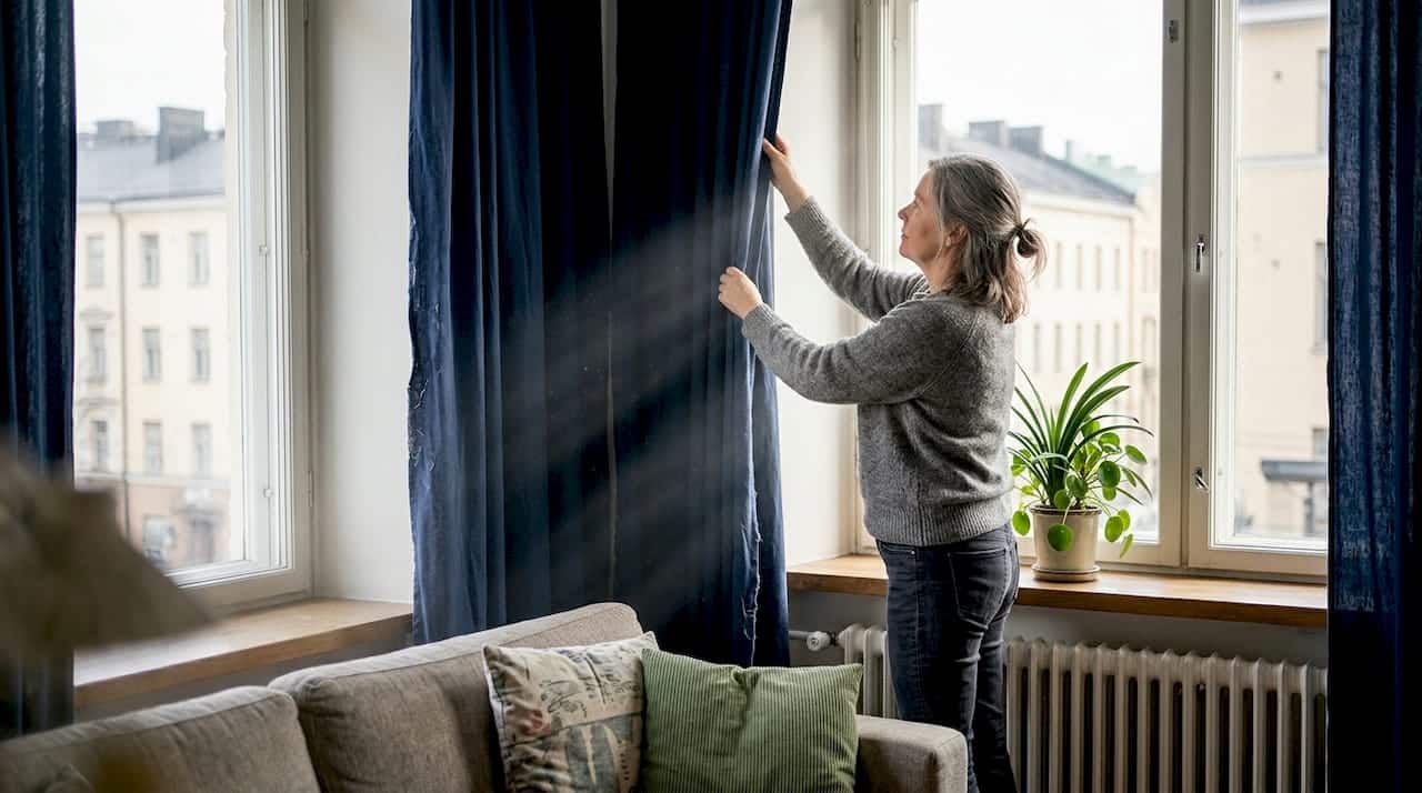Nainen säätää verhoja parantaakseen kodin energiatehokkuutta.